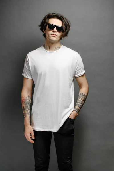 Hipster handsome male model with glasses wearing white blank t-shirt and black jeans with space for your logo or design in casual urban style — Stock Photo, Image