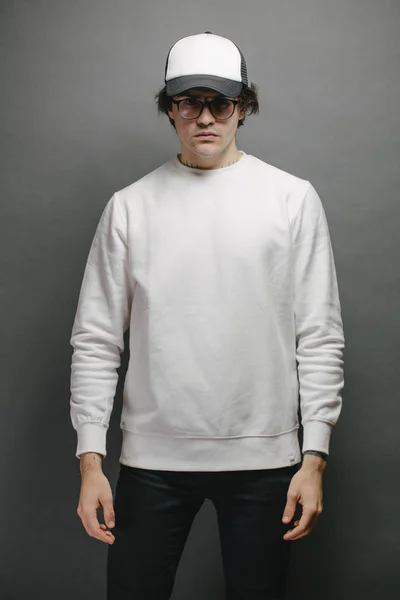Een man met een wit sweatshirt en een lege honkbalpet over een grijze achtergrond. Sweatshirt of hoodie voor mock up, logo designs of design print met vrije ruimte. — Stockfoto