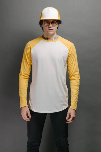 Modelo de hombre con barba en blanco y amarillo en blanco Camisa de manga larga para maqueta y gorra de béisbol con espacio para su logotipo o diseño sobre fondo gris —  Fotos de Stock