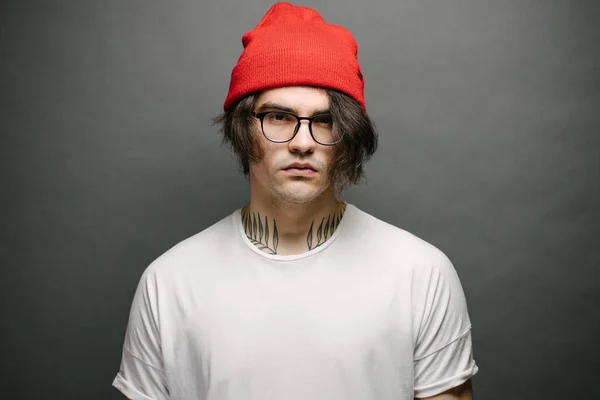 Hipster knap mannelijk model met bril in wit wit wit t-shirt en rode broek en een rode muts met ruimte voor uw logo of ontwerp over grijze achtergrond — Stockfoto