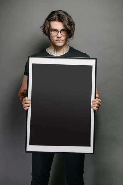 Férfi kezében egy képkeret vagy poszter gúnyolódni visel fekete ruhát — Stock Fotó