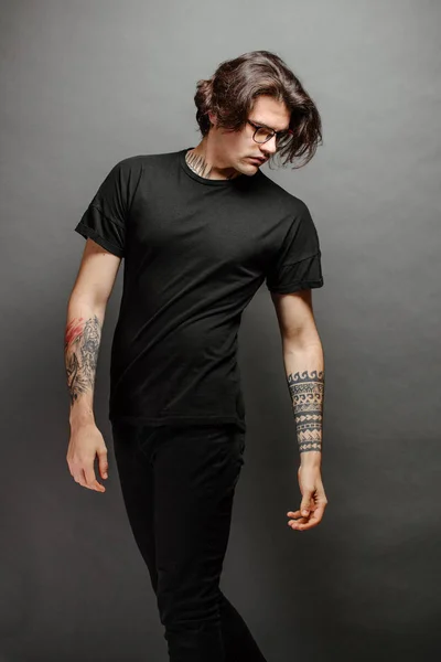 Hipster knappe mannelijke model met bril dragen zwarte witte t-shirt en zwarte jeans met ruimte voor uw logo of ontwerp in casual stedelijke stijl — Stockfoto