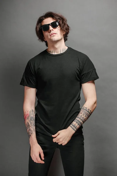 Hipster guapo modelo masculino con gafas con camiseta en blanco negro y jeans negros con espacio para su logotipo o diseño en estilo urbano casual —  Fotos de Stock