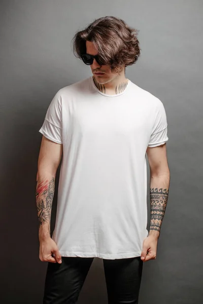 Hipster guapo modelo masculino con gafas en blanco camiseta en blanco y vaqueros negros con espacio para su logotipo o diseño en estilo urbano casual —  Fotos de Stock