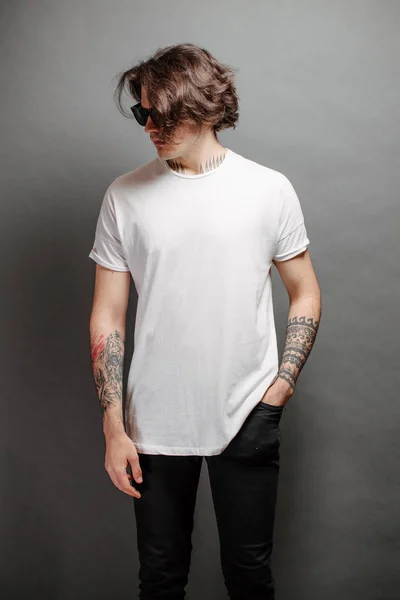 Hipster handsome male model with glasses wearing white blank t-shirt and black jeans with space for your logo or design in casual urban style — Stock Photo, Image
