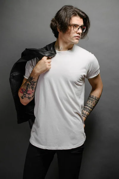 Hipster guapo modelo masculino con gafas en blanco camiseta en blanco y vaqueros negros con espacio para su logotipo o diseño en estilo urbano casual —  Fotos de Stock