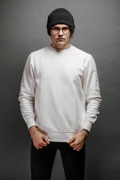 Man wearing white sweatshirt and a black hat standing over gray background. Sweatshirt or hoodie for mock up, logo designs or design prints with with free space