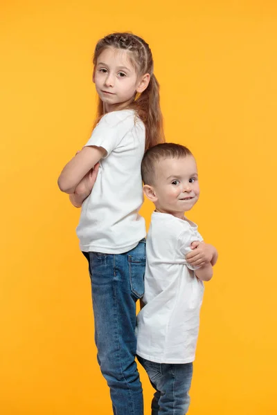 Sister and brother portraits over yellow background. They are wearing white t-shirts — Stock Photo, Image