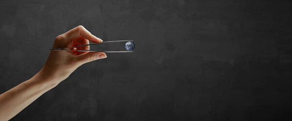 Hands holding planet in a tweezers over gray background