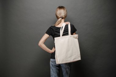 Gri arka plan karşı beyaz tekstil eko çanta tutan genç kadın. Ekoloji veya çevre koruma kavramı. Sahte için beyaz eko çanta.
