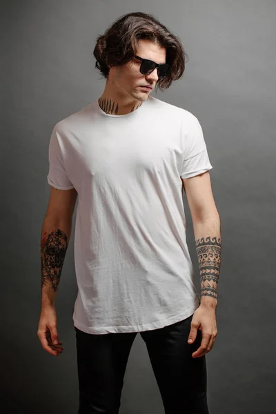 Hipster handsome male model with glasses wearing white blank t-shirt and black jeans with space for your logo or design in casual urban style — Stock Photo, Image