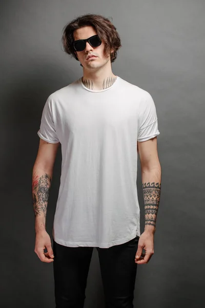 Modelo masculino bonito Hipster com óculos vestindo camiseta branca em branco e jeans pretos com espaço para o seu logotipo ou design em estilo urbano casual — Fotografia de Stock