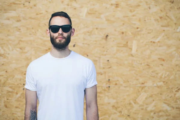 Hipster handsome male model with beard wearing white blank t-shirt and sunglasses and beard with space for your logo or design in casual urban style — Stock Photo, Image