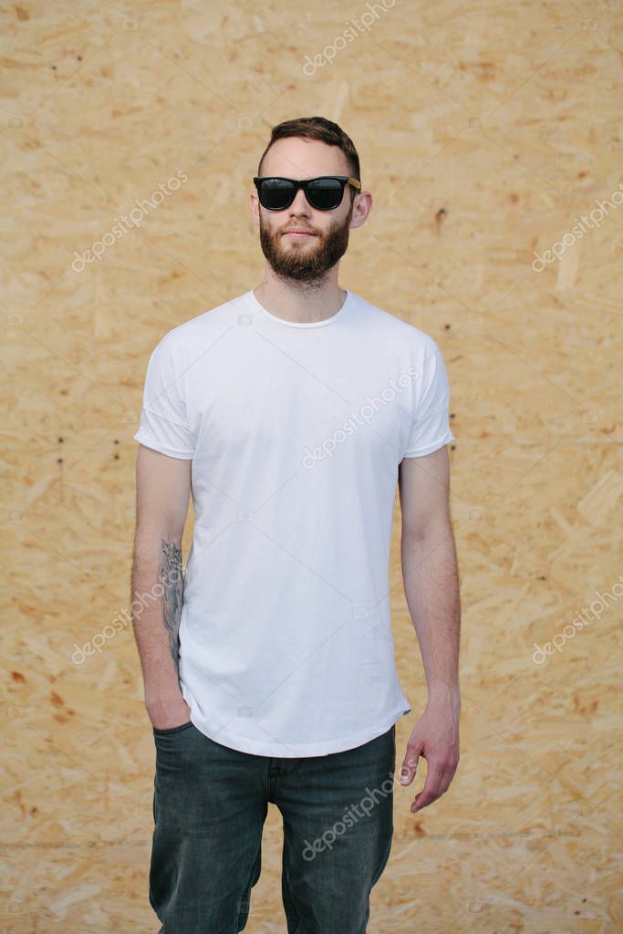 Hipster handsome male model with beard wearing white blank t-shirt and sunglasses and beard with space for your logo or design in casual urban style