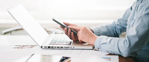 Desenvolvedor de site trabalhando usando laptop no escritório em mesa de madeira. Ela está usando um celular — Fotografia de Stock