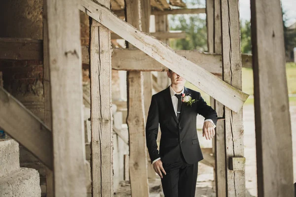 Fashion portrait of a groom outside. Half of his face is hidden behind a wooden plank — 스톡 사진