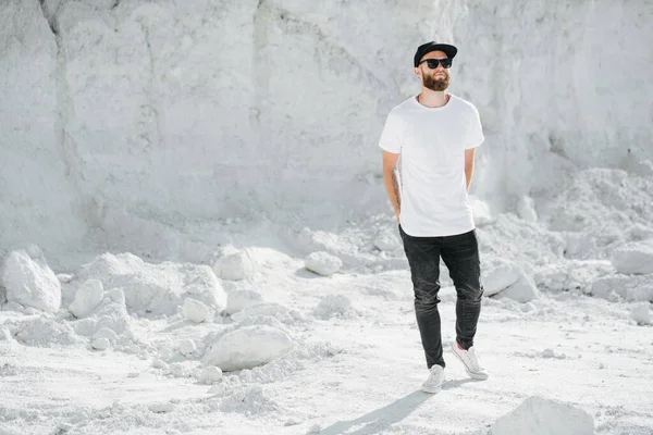 Hipster handsome male model with beard wearing white blank t-shirt and a baseball cap with space for your logo or design in casual urban style — Stock Photo, Image