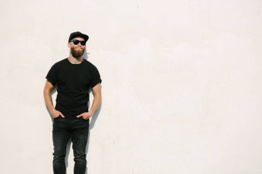 Sakallı, siyah, boş tişörtlü, beysbol şapkalı, logonuz için yeri olan yakışıklı bir hippi mankeni.