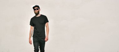 Sakallı, siyah, boş tişörtlü, beysbol şapkalı, logonuz için yeri olan yakışıklı bir hippi mankeni.