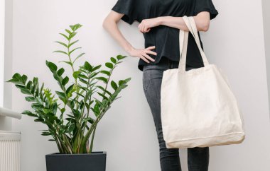 Beyaz duvara beyaz tekstil eko çanta tutan genç bir kadın. Ekoloji ya da çevre koruma kavramı. Model için beyaz eko çanta.