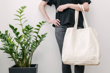 Beyaz duvara beyaz tekstil eko çanta tutan genç bir kadın. Ekoloji ya da çevre koruma kavramı. Model için beyaz eko çanta.