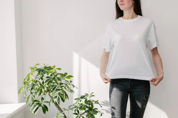 Skinny woman wearing white blank t-shirt and black jeans with space for your logo or design in casual urban style over white wall