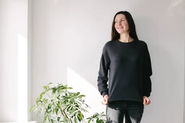 Woman wearing black sweatshirt standing over white wall background. Sweatshirt or hoodie for mock up, logo designs or design prints with with free space