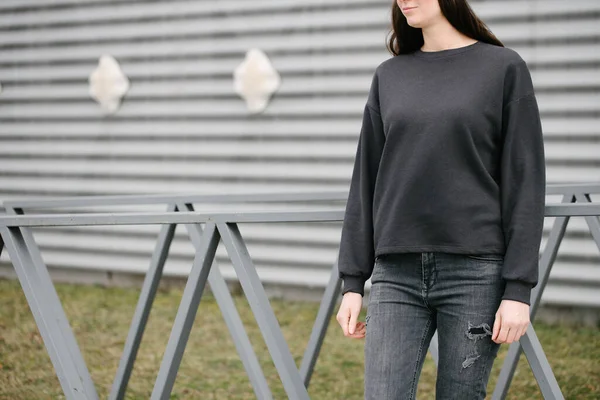 Woman wearing black sweatshirt standing in urban area in casual urban style over gray background. Sweatshirt or hoodie for mock up, logo designs or design prints with with free space