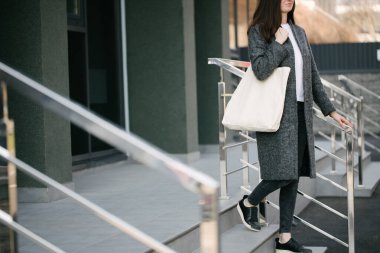 Şehrin arka planında beyaz tekstil eko çantası tutan genç bir kadın. Ekoloji ya da çevre koruma kavramı. Model için beyaz eko çanta