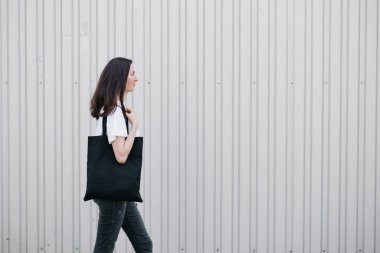 Şehir geçmişine karşı siyah tekstil eko çantası taşıyan genç bir kadın. Ekoloji ya da çevre koruma kavramı. Model için beyaz eko çanta