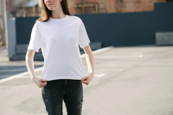穿着白色空白T恤和黑色牛仔裤的瘦瘦的女人 在城市街道的背景下 为你的标志或设计出休闲的都市风格 — 图库照片