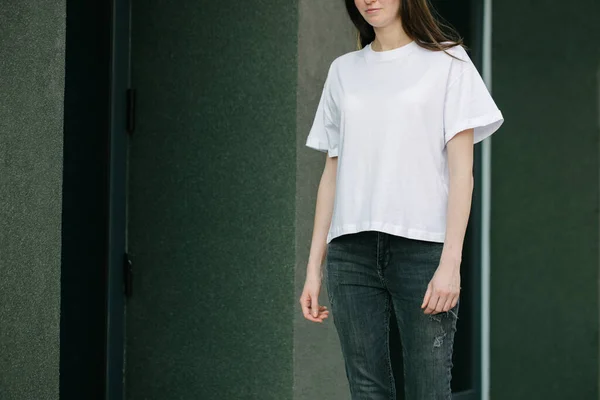 あなたのロゴやデザインのためのスペースと白い空白のTシャツと黒のジーンズを身に着けているスキニー女性は 都市の通りの背景にカジュアルな都市スタイルで — ストック写真