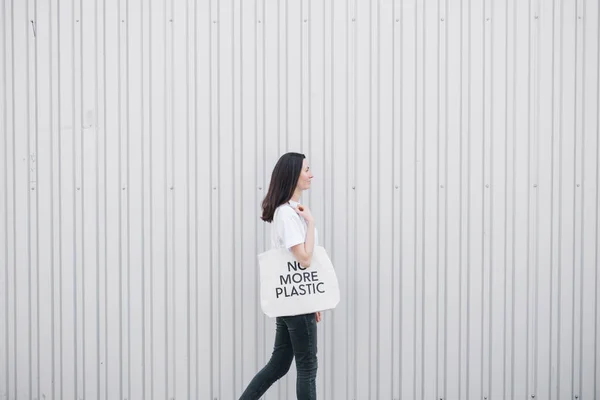 No more plastic eco concept of woman holding white textile eco bag against metal wall background. Ecology or environment protection concept. White eco bag for mock up.