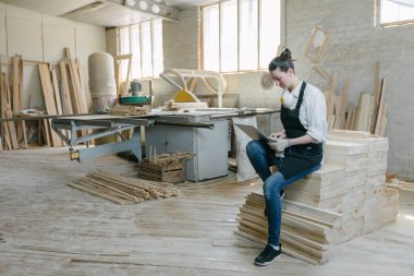 Kendi marangozhanesinde marangoz olarak çalışan kendine güvenen bir kadın. Dizüstü bilgisayar kullanıyor ve çalışma odasındayken notlar yazıyor. Küçük işletme kavramı.