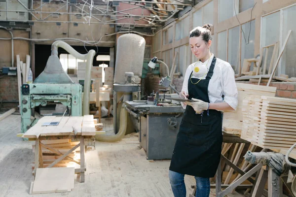 自信的女人在自己的木材店里做木匠 她在工作时使用平板电脑并写笔记 小企业概念 — 图库照片