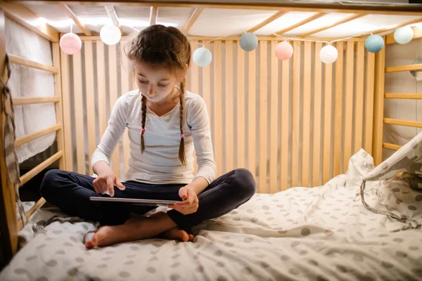 Dziecko Ogląda Tablet Domu Dziewczyna Ogląda Tablet Siedzi Łóżku Girlandy — Zdjęcie stockowe