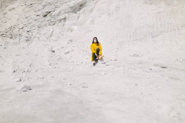 Kimyasal bitki atıklarının oluşturduğu fosfat dağında yürüyen genç bir kadın. Sarı koruyucu ceket ve maske giyiyor. Ekoloji koruma farkındalığı
