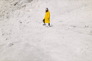 Kimyasal bitki atıklarının oluşturduğu fosfat dağında yürüyen genç bir kadın. Sarı koruyucu ceket ve maske giyiyor. Ekoloji koruma farkındalığı