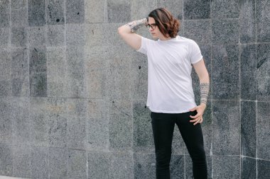 Hippi yakışıklı erkek manken beyaz boş tişört giyiyor. Logonuz için yeri var. Ya da şehir tarzı tasarım.