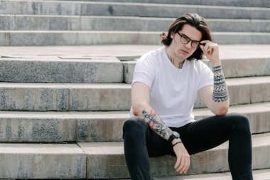 Hippi yakışıklı erkek manken beyaz boş tişört giyiyor. Logonuz için yeri var. Ya da şehir tarzı tasarım.