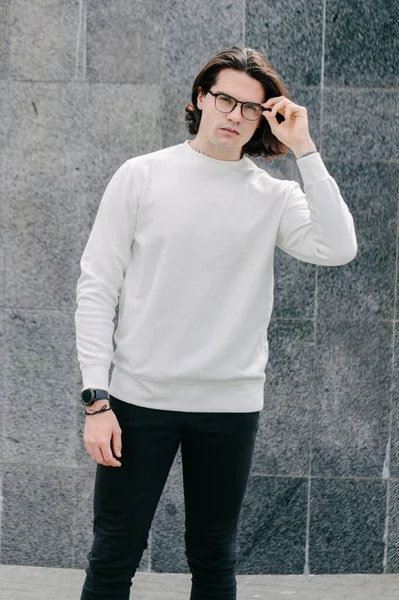 Man wearing white sweatshirt or hoodie and glasses outside on the city streets. Sweatshirt or hoodie for mock up, logo designs or design prints with free space