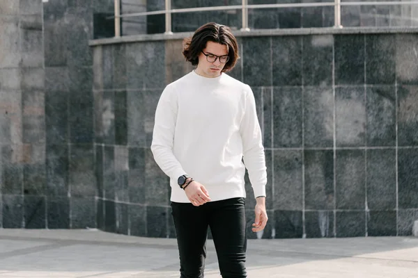 Man wearing white sweatshirt or hoodie and glasses outside on the city streets. Sweatshirt or hoodie for mock up, logo designs or design prints with free space