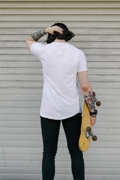 あなたのロゴやデザインのためのスペースと白い空白のTシャツを身に着けているヒップスターハンサムな男性モデルカジュアルな都市スタイルで スケートボードを持ってる — ストック写真