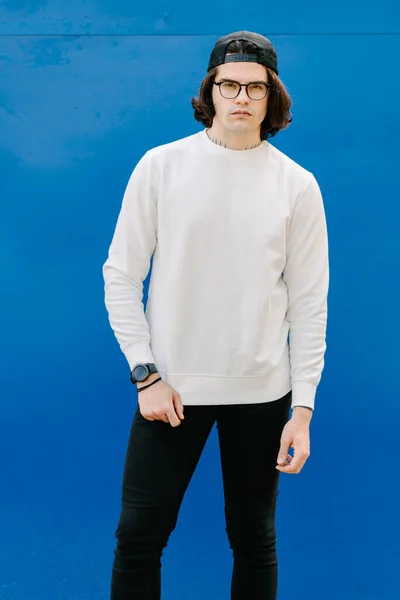 Man wearing white sweatshirt or hoodie and glasses outside over blue background. Sweatshirt or hoodie for mock up, logo designs or design prints with free space
