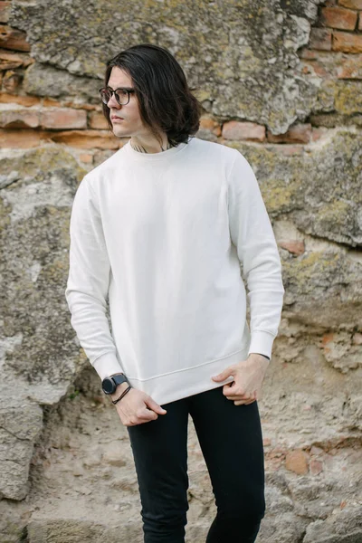 Man wearing white sweatshirt or hoodie and glasses outside on the city streets. Sweatshirt or hoodie for mock up, logo designs or design prints with free space.