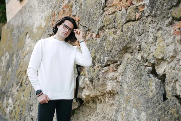 Man wearing white sweatshirt or hoodie and glasses outside on the city streets. Sweatshirt or hoodie for mock up, logo designs or design prints with free space.