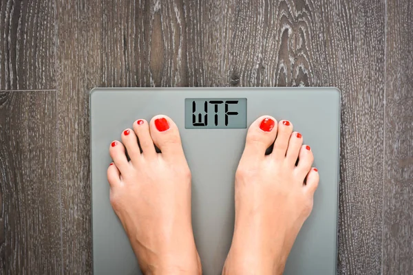 Conceito de dieta com pés de mulher em uma escala exibindo palavra WTF — Fotografia de Stock