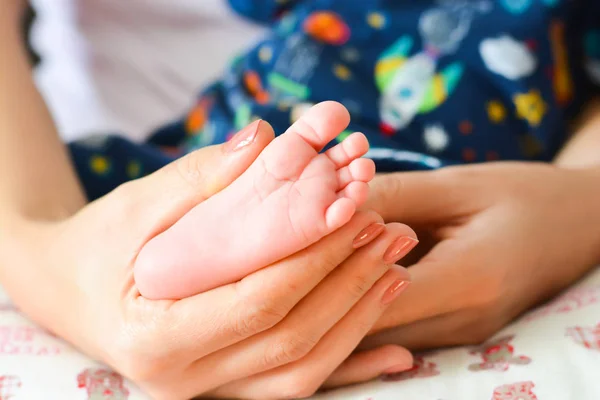 彼女の手のひらで生まれたばかりの赤ちゃんの足を保持している若い母親 — ストック写真