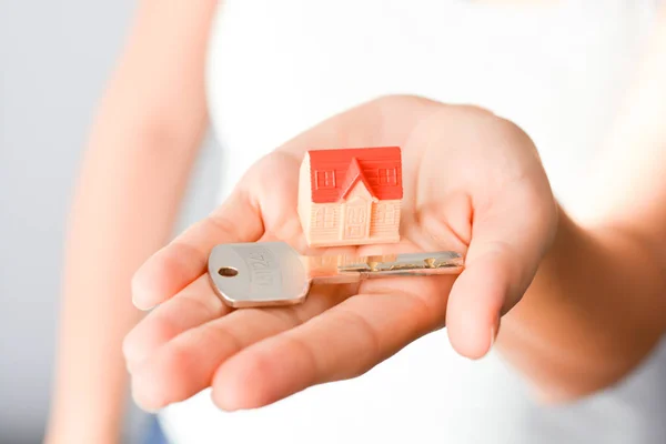 Крупный план женских рук, держащих небольшой образцовый дом и ключ, предполагающий приобретение или аренду дома — стоковое фото
