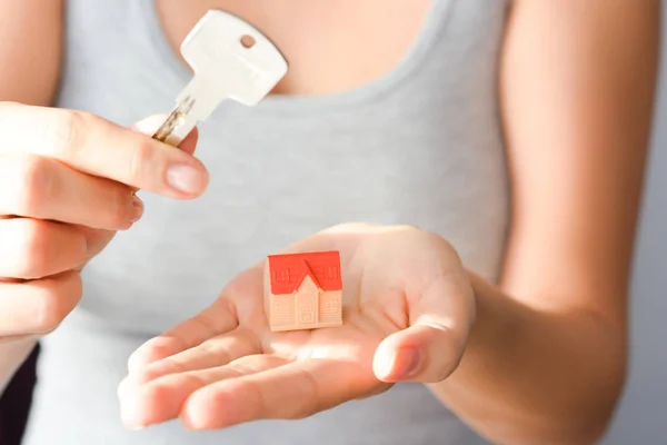 Primer plano de las manos de una mujer sosteniendo una pequeña casa modelo y una llave que sugiere la adquisición o alquiler de una casa —  Fotos de Stock